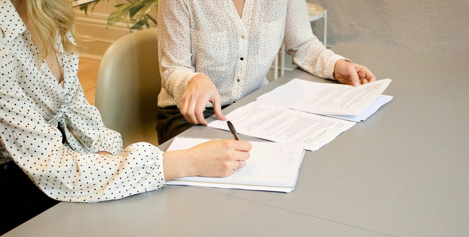 woman signing on white printer paper beside woman about to touch the documents